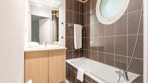 A modern bathroom with a wooden vanity, a large mirror, a round mirror, a bathtub, and tiled walls. - Les Carrelets 3 Bedroom Split-level APT (Saint-Palais-sur-Mer)