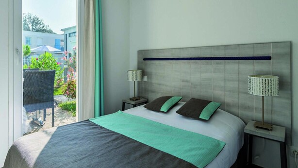 A hotel room with a bed, two bedside tables, a headboard, and a view of the outside. - Les Carrelets 3 Bedroom Split-level APT (Saint-Palais-sur-Mer)