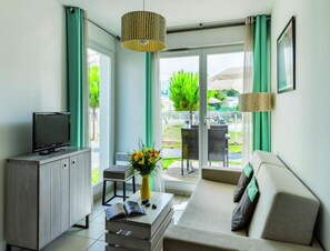 A modern living room with a sofa, a TV on a cabinet, a small table with a vase of flowers, and a view of the outdoors. - Les Carrelets 3 Bedroom Split-level APT (Saint-Palais-sur-Mer)
