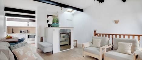Una sala de estar moderna con sofá, sillones, una mesa de centro y una cocina al fondo.