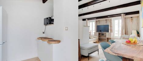 Una cocina moderna con vigas de madera, un comedor con mesa y sillas, y una sala de estar con sofá y televisor.