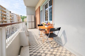 A balcony with a checkered floor, a table with chairs, a vase of flowers, and a view of apartment buildings. - Elegantis.it Scalia Comfortable Apartment (Roma)