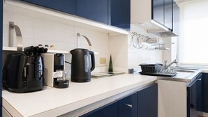 Una cucina moderna con mobili blu scuro, un piano di lavoro bianco, una macchina da caffè, un bollitore e un espositore per piatti.