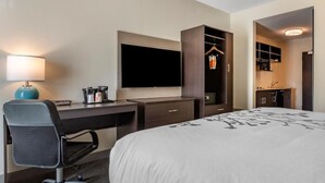 A hotel room with a bed, desk, chair, TV, wardrobe, and a kitchenette.