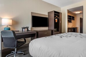 Una habitación de hotel con cama, escritorio, silla, televisión, armario y kitchenette.