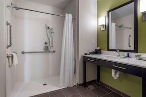 A bathroom with a shower, grab bars, a sink, and a mirror.