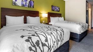 A hotel room with two beds, a green accent wall, and floral artwork.