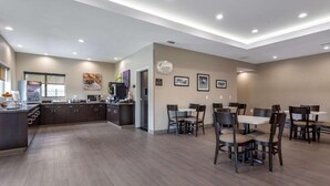 A spacious dining area with multiple tables and chairs, a kitchen area with modern appliances, and framed artwork on the walls.