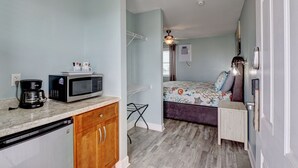 Ein kompakter Raum mit Küchenzeile, einem Bett mit bunter Bettdecke, einem kleinen Tisch und einem Deckenventilator.