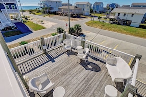 A wooden deck with white wicker furniture, a railing, and a view of the surrounding neighborhood.