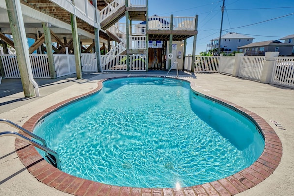 A swimming pool with a wooden deck, a staircase, and a white fence.