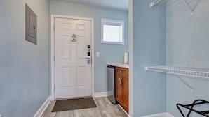 A hallway with a white door, a small window, a kitchen area with a dishwasher, and a metal shelf. - Surf City Stay – Motel Unit - Walk to Beach (Surf City)