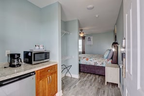 Una habitación compacta con kitchenette, una cama con colcha colorida, una mesita y un ventilador de techo.