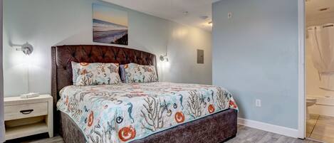 A bedroom with a bed, nightstand, ceiling fan, and a view of the bathroom.