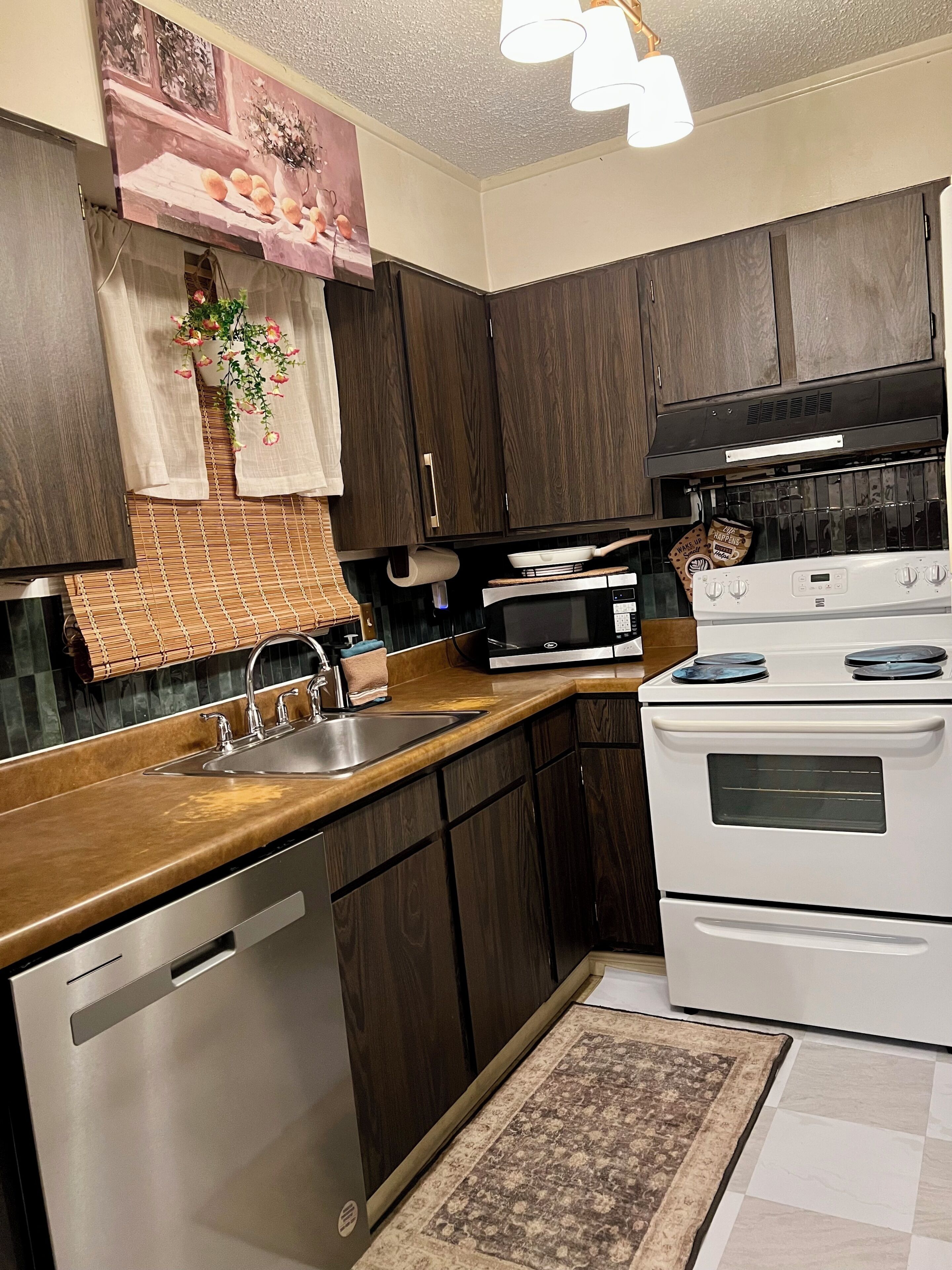 A kitchen with dark wood cabinets, a stainless steel dishwasher, a white stove, and a microwave.