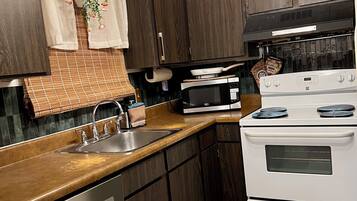 A kitchen with dark wood cabinets, a stainless steel dishwasher, a white stove, and a microwave.