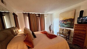 Een hotelkamer met een groot bed, een televisie, een schilderij aan de muur en een raam met gordijnen.