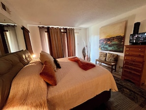 A hotel room with a large bed, a television, a painting on the wall, and a window with curtains. - Condo • 2 Beds •1 ba near Downtown-Riverwalk, La cantera-Fiesta Texas, Sea World (San Antonio)