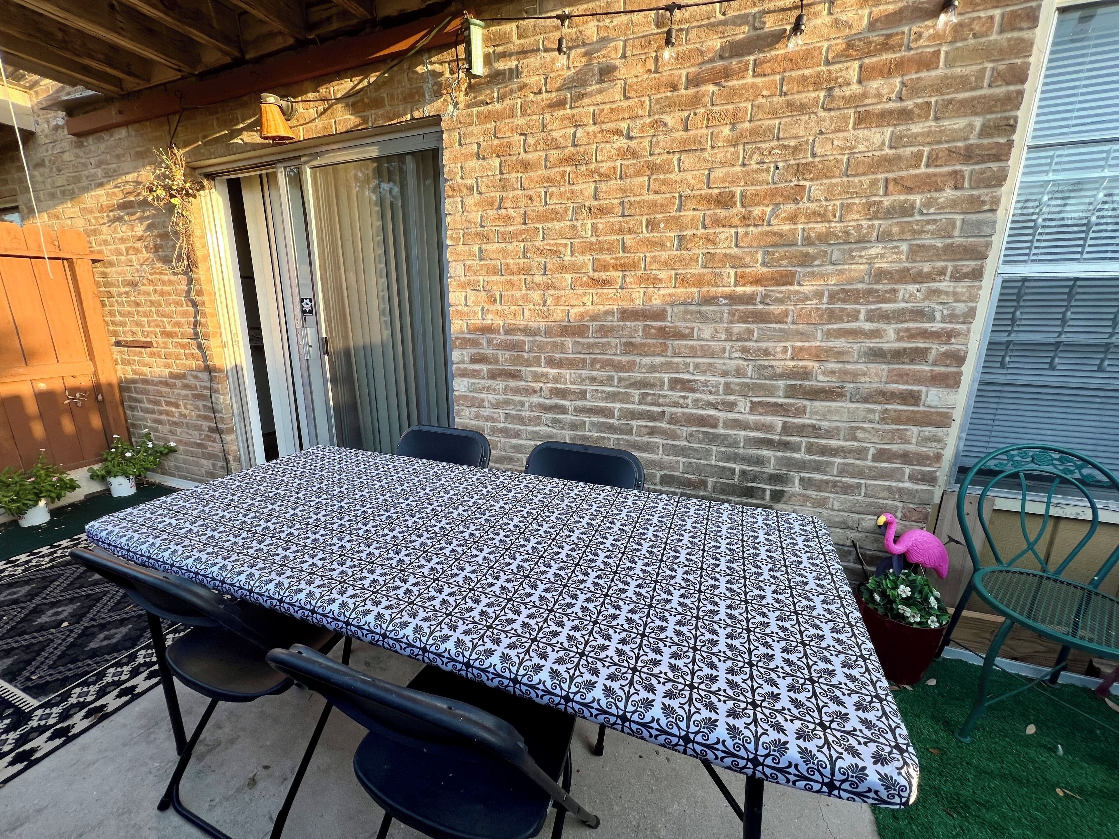 A patio with a table and chairs, a brick wall, a wooden door, and a green chair.