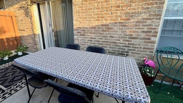 A patio with a table and chairs, a brick wall, a wooden door, and a green chair.