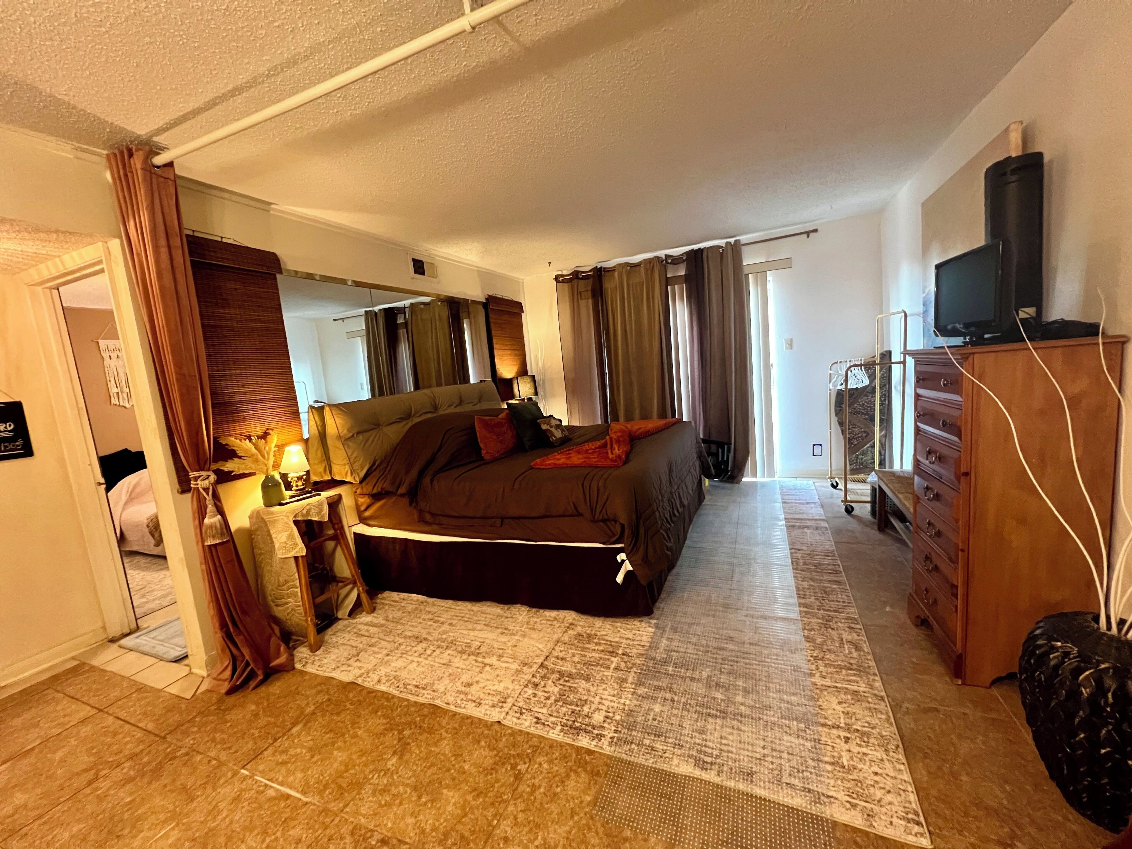 Een slaapkamer met een bed, een kaptafel, een televisie en een raam met gordijnen.