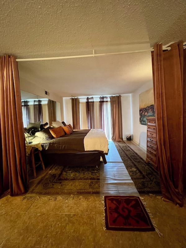 Una habitación de hotel con cama, escritorio, silla, cómoda y alfombra estampada.