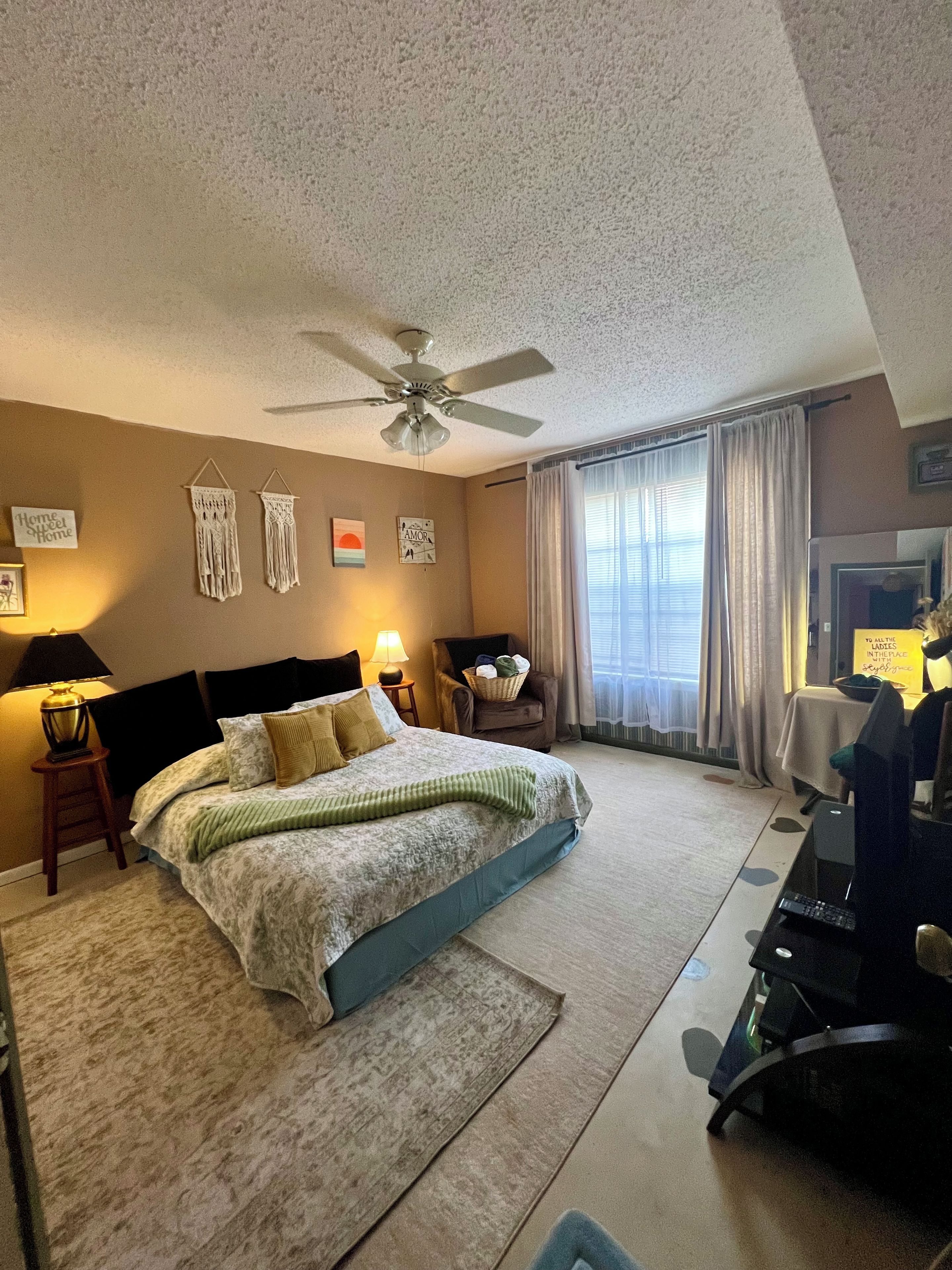 A hotel room with a bed, a desk, a chair, a ceiling fan, and a window with curtains.