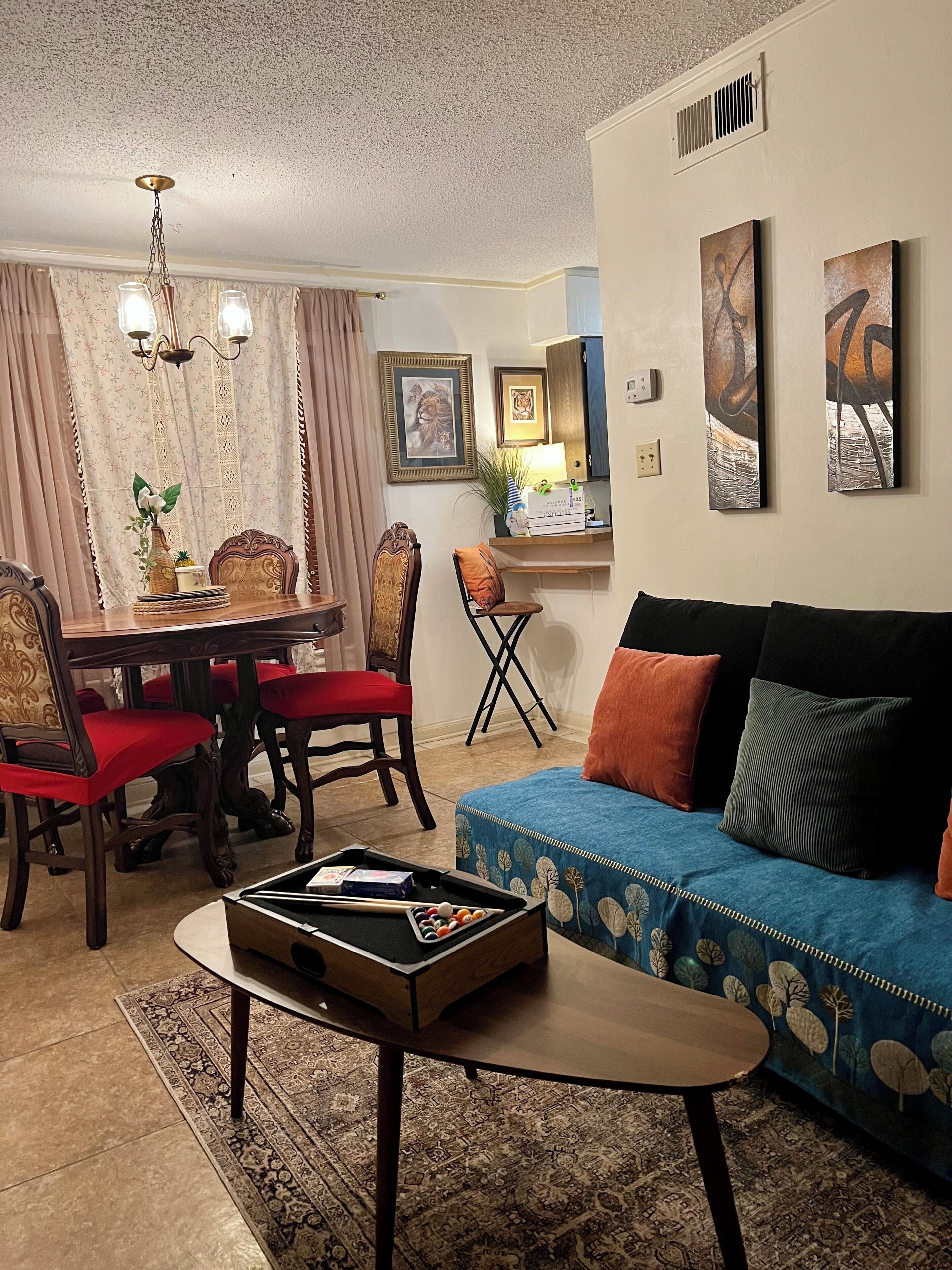 A living room with a pool table, a sofa with cushions, a dining area with chairs, and artwork on the walls.