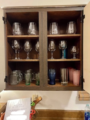 Un meuble en bois doté d’étagères où sont rangés divers objets en verre et différentes tasses.