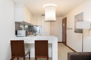 Ein Hotelzimmer mit Küchenzeile, einer Essecke mit zwei Stühlen, einer großen weißen Lampe und einem Gemälde an der Wand.