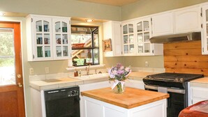 Una cocina con armarios blancos, lavavajillas, estufa y ventana con vistas a zonas verdes.