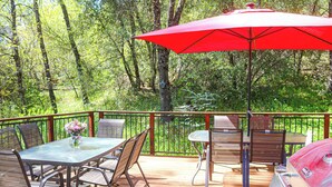 Una terraza con mesa de vidrio, sillas, una sombrilla roja y una parrilla.