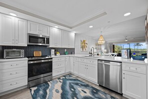 A modern kitchen with white cabinets, stainless steel appliances, a patterned backsplash, and a blue rug.
