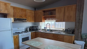 A kitchen with wooden cabinets, a white refrigerator, a stove, a microwave, a sink, and a window.