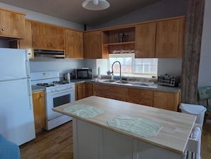 Une cuisine avec des meubles de rangement en bois, un réfrigérateur blanc, une cuisinière, un four à micro-ondes, un évier et une fenêtre.