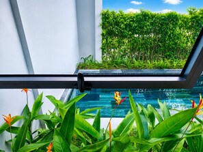 A modern indoor pool with clear glass walls, surrounded by lush tropical plants and a view of a dense green hedge outside. - Kalia Villa (Phu Quoc)