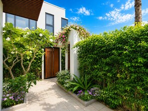 A modern building with a wooden door, surrounded by lush greenery and flowering plants. - Kalia Villa (Phu Quoc)