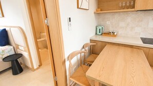 Cozinha compacta com uma mesa de madeira, cadeiras, chaleira e um pequeno balcão.
