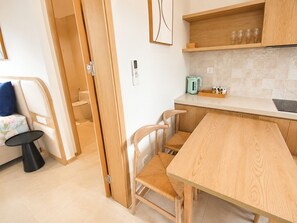 A compact kitchen with a wooden table, chairs, a kettle, and a small countertop. - Kalia Villa (Phu Quoc)