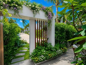 A gated entrance with a white archway, lush greenery, and a clear sky. - Kalia Villa (Phu Quoc)