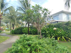 A lush garden with palm trees, a pathway, and a modern building in the background. - Kalia Villa (Phu Quoc)