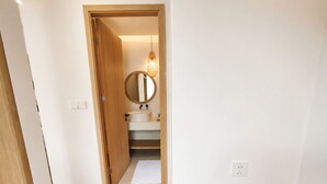 Um quarto com piso de madeira, uma mesa pequena e uma porta que dá para um banheiro com espelho redondo e pia.