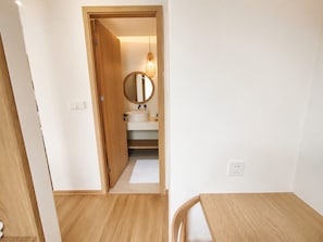 A room with a wooden floor, a small table, and a door leading to a bathroom with a round mirror and a sink. - Kalia Villa (Phu Quoc)