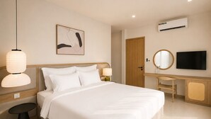 Quarto de hotel com cama, mesa de cabeceira, luminária, obra de arte, escrivaninha, cadeira, televisão e aparelho de ar condicionado.