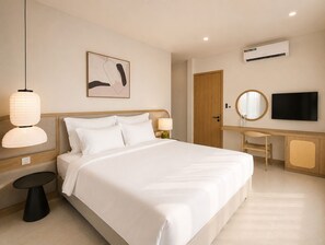 A hotel room with a bed, bedside table, lamp, artwork, desk, chair, television, and an air conditioning unit. - Kalia Villa (Phu Quoc)