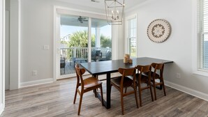 A dining area with a dark wooden table and four chairs, a chandelier, and a decorative wall piece. - Lucky Snapper - Walk to Beach & Tiki Bar, Pets Ok (Carolina Beach)