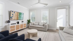 A modern living room with a white sofa, a round coffee table, and a TV mounted on the wall. - Lucky Snapper - Walk to Beach & Tiki Bar, Pets Ok (Carolina Beach)