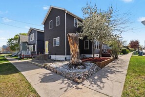 Une maison d’habitation avec un jardin devant, un arbre et un trottoir.