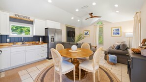 A modern kitchen with white cabinets, a dining table with chairs, a refrigerator, and a ceiling fan. - Nautigull- A Fisherman's Delight (Apalachicola)