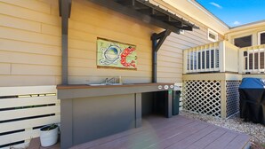 An outdoor kitchen with a sink, a grill, and a decorative painting on the wall. - Nautigull- A Fisherman's Delight (Apalachicola)